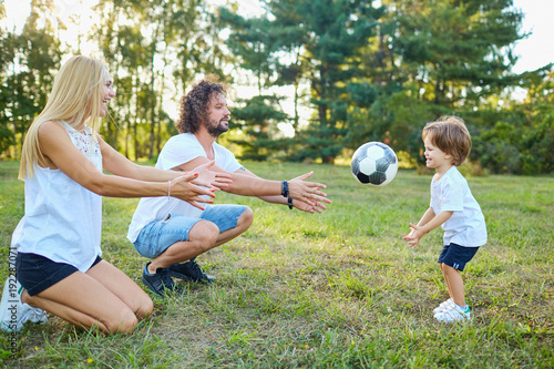 Family playing with a ball in the park. Parents with son on grass in nature.