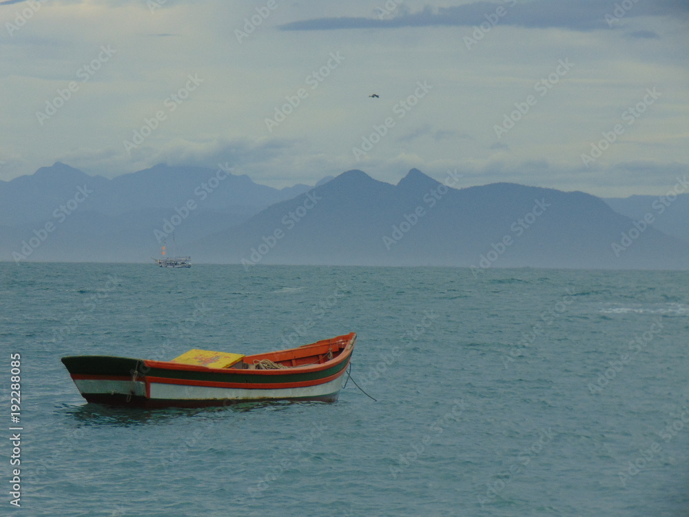 barca colorida en mar azul calmo con un fondo de montañas y cielo que transmite calma