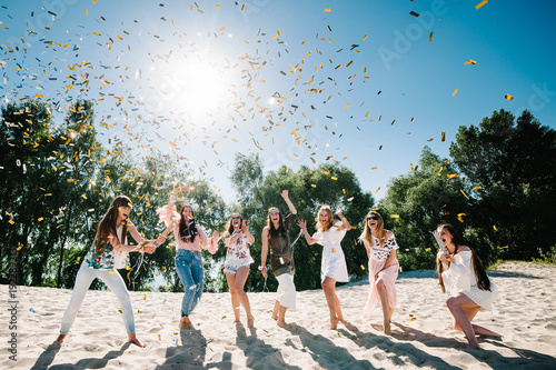 Canvas Print Beautiful happy stylish sexy young girls stand in beach and opens colored confetti on background nature