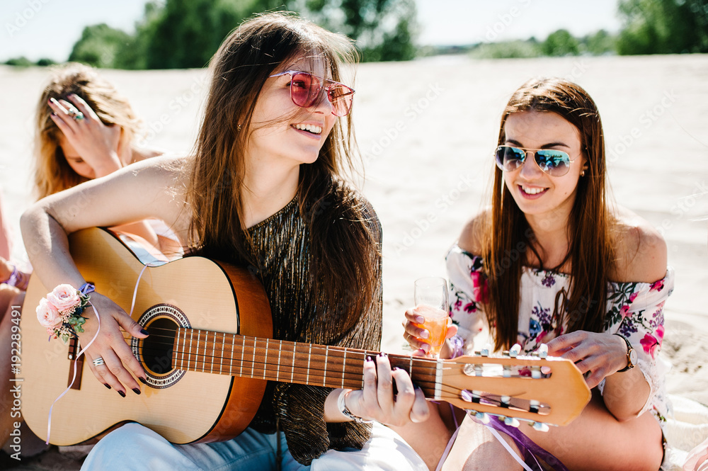 Beautiful happy slim stylish sexy young girl sitting sand beach drink champagne Play guitar. hand decorated with ribbons flowers. Party. Style boho. Maiden evening Hen-parties. Bachelorette. Close up