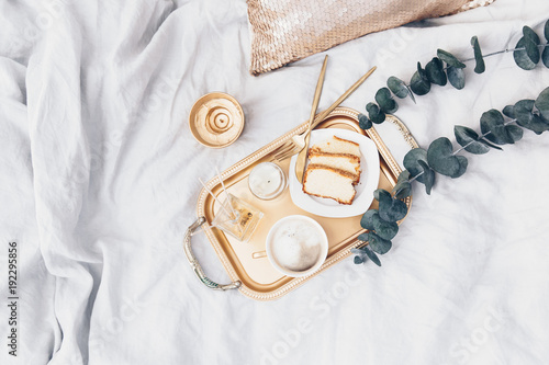 Gold tray with coffee and eucalyptus on clean white bedding. Good morning concept. Flat lay photo