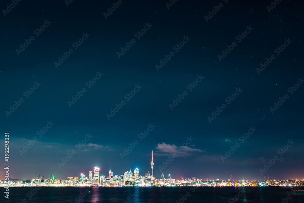 Fototapeta premium Clear starry sky above Auckland city’s skyline with the harbour, the ocean and some boats at the front