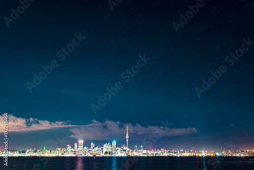 Clear starry sky above Auckland city’s skyline with the harbour, the ocean and some boats at the front © ydumortier