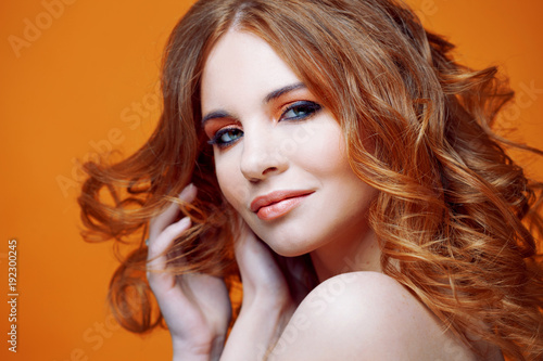 Happy redheaded young woman with luxurious curly hair. Studio portrait on yellow background. Excellent hair