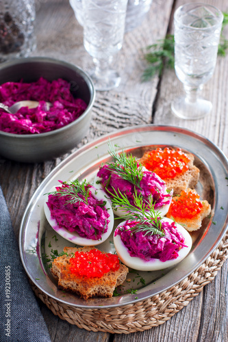 Snack of stuffed eggs with beets and fish filling on a wooden table, rustic style, selective focus