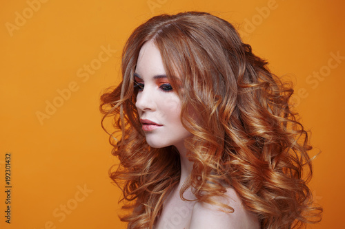 Beautiful redheaded girl with luxurious curly hair. Studio portrait on yellow background. Excellent hair
