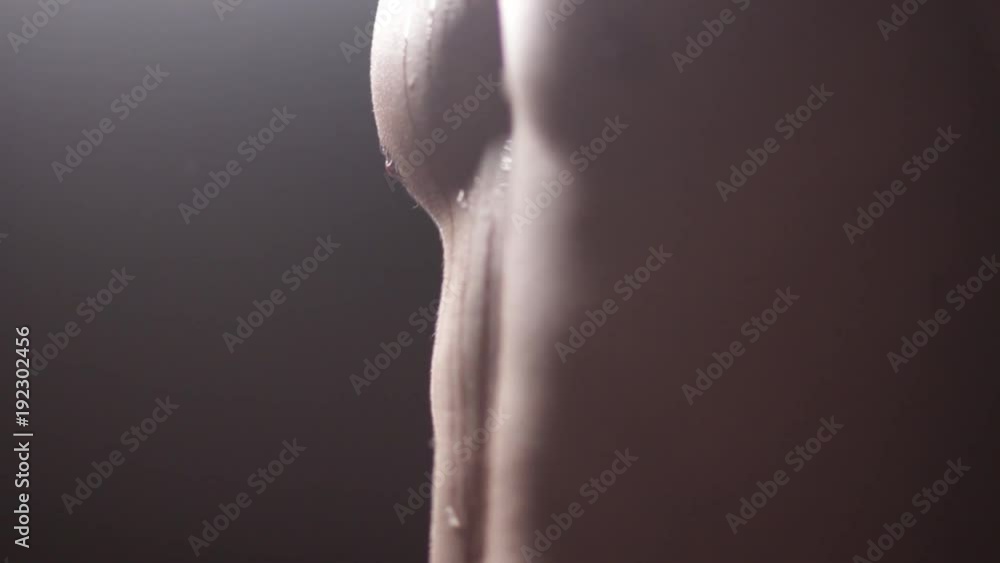 Drops of sweat or rain flow down the male body. Close-up of an athlete's chest on a dark background. Modeling light. For sports screensavers or news. Drops of sweat or rain flow down the male body. Close-up of an athlete's chest on a dark background. Modeling light. For sports screensavers or news.