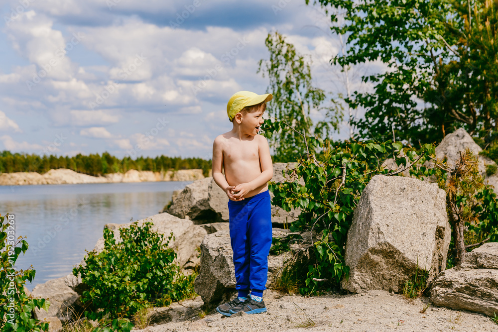 boy in a cap stands on rocky shore on Sunny summer day