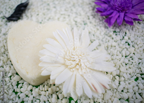 White heart from soap and white flower on a light background of small stones.