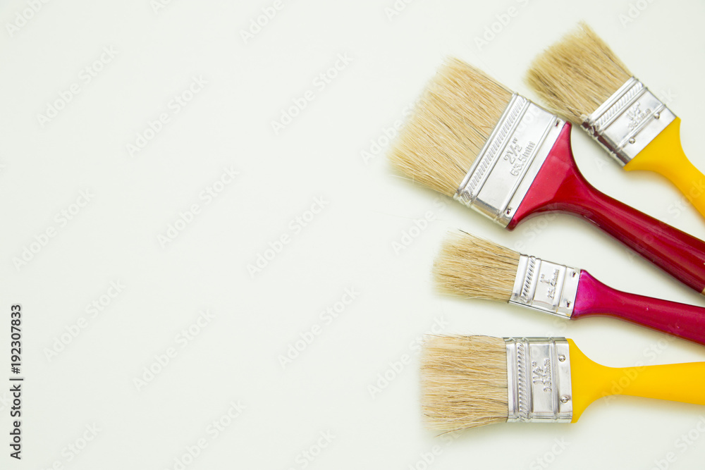 Fototapeta premium Painting the house. Two red and two yellow paint brushes on white background with copy space, top view, flat lay