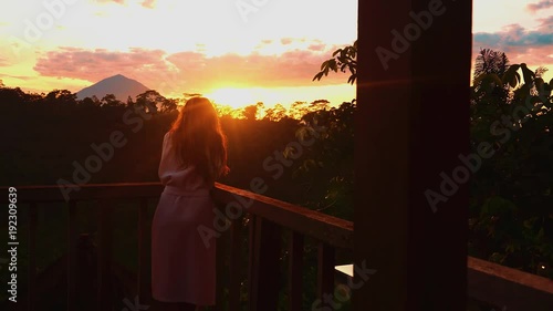 Tourist woman looking out at view from hotel balcony at sunise volcano in tropical forest Independent female traveller enjoying relaxed lifestyle on summer vacation in Asia photo