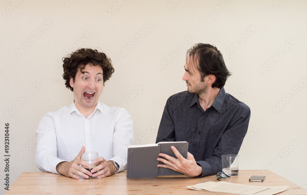 Two young Caucasian colleagues discussing at the table in the office with light background. Two young Caucasian colleagues discussing at the table in the office with light background.