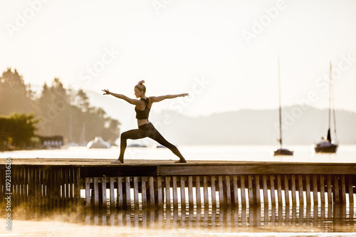 Woman practicing yoga on jetty at a lake photo