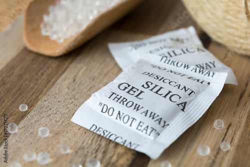 Desiccant or silica gel in white paper packaging and spread on the wooden background.