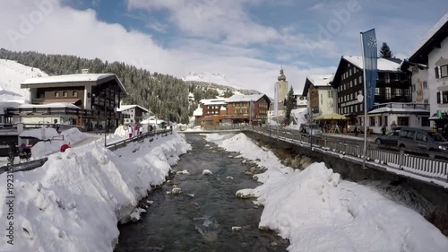 Stream trough ski village Lech in Tyrol, Austria, with skiers walking an view at church photo
