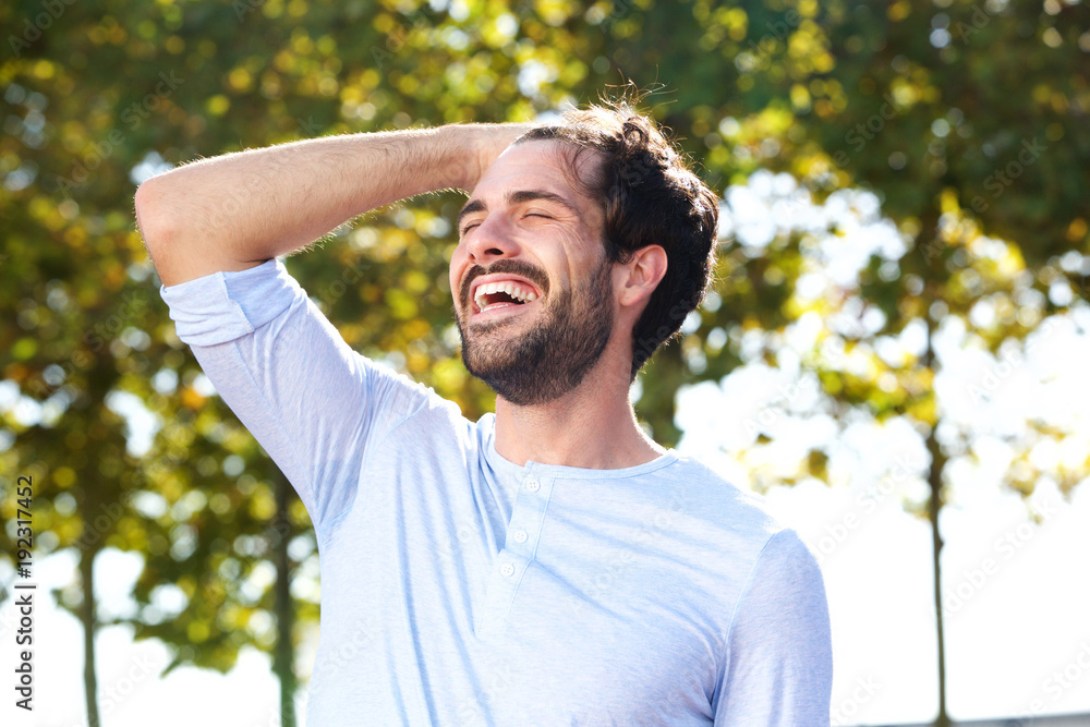 Fototapeta premium happy young man smiling outdoors with hand in hair