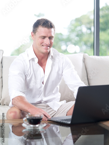 portrait of young man sitting on sofa with laptop in summer house environment