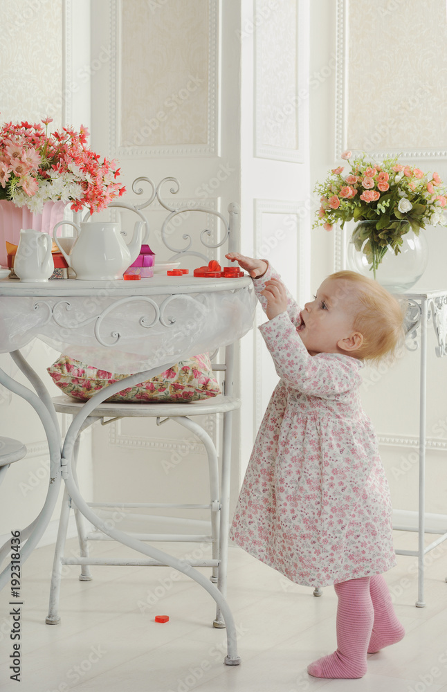 Little girl in dress near table for tea, in interior Little girl in dress near table for tea, in interior