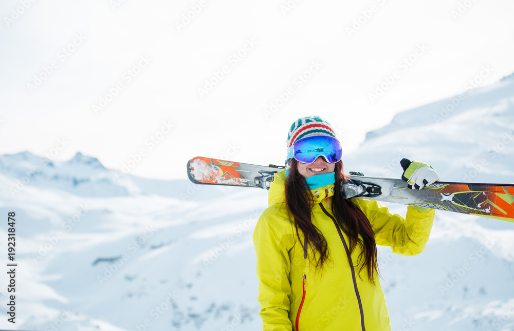 Picture of athlete woman with skis on her shoulder against background of snowy hill