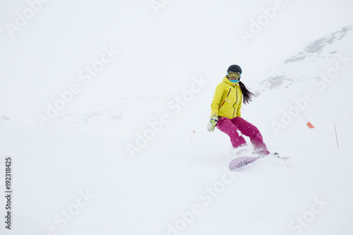 Image of athlete girl in helmet with developing hair, snowboarding from mountain slope