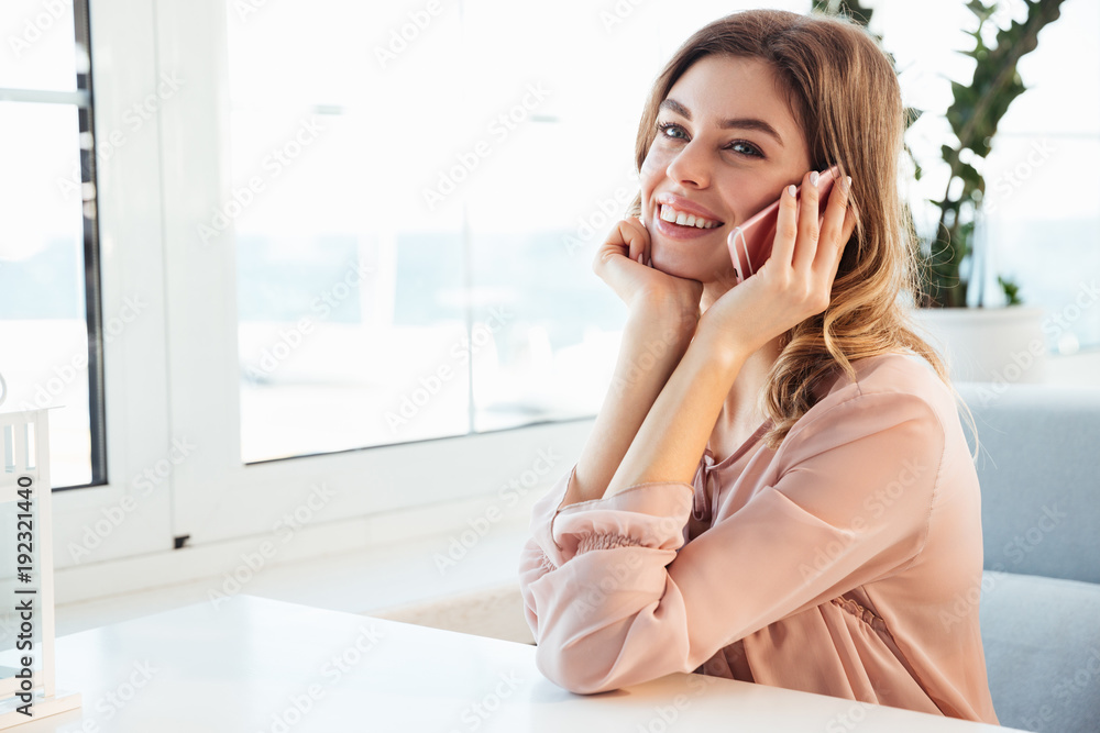 Fototapeta premium Smiling blondy woman in blouse sitting by the table