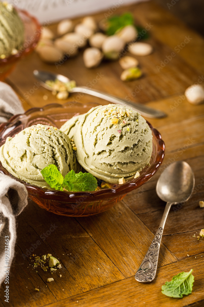 Pistachio ice cream scoops with grated pistachos in red glass bowl on old wooden table background. Homemade summer food concept with copy space. Pistachio ice cream scoops with grated pistachos in red glass bowl on old wooden table background. Homemade summer food concept with copy space.