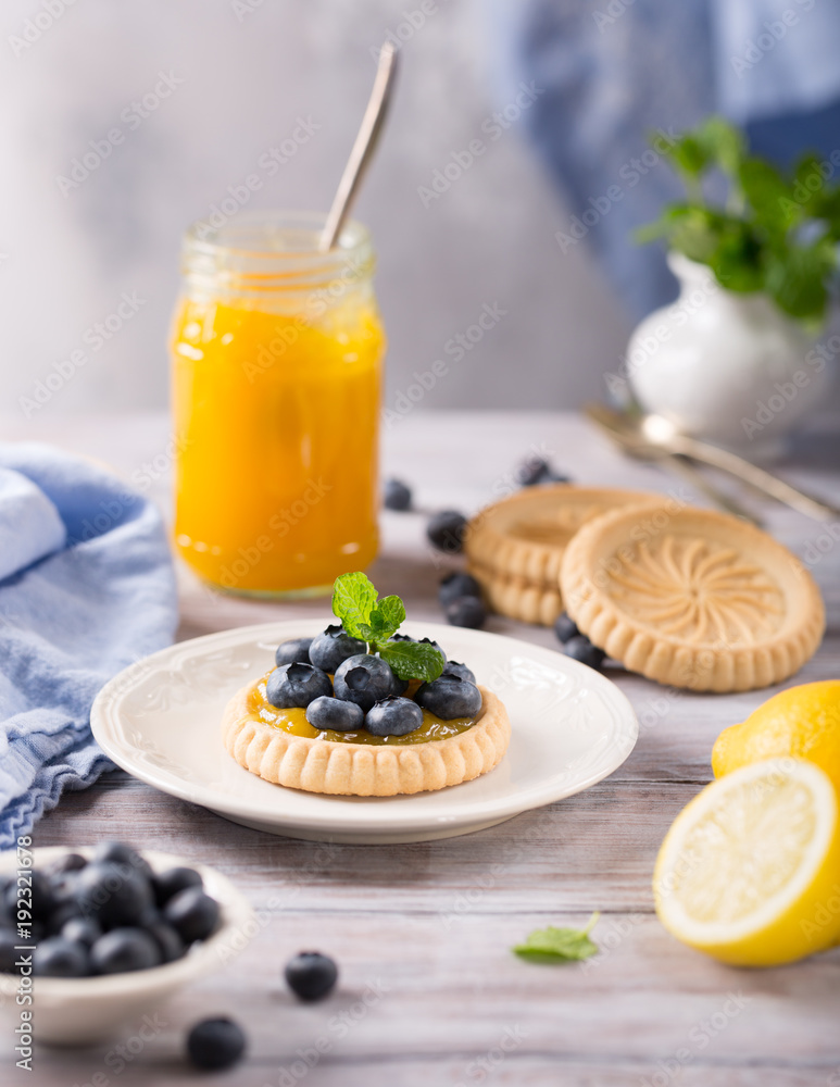 Homemade shortbread tartlet with lemon curd and fresh blueberries on white wooden background. Holiday food concept with copy space. Homemade shortbread tartlet with lemon curd and fresh blueberries on white wooden background. Holiday food concept with copy space.