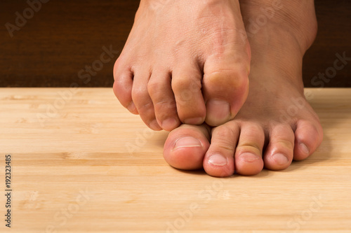 Close up a man with itchy feet uses his big toe to scratch his other foot on wooden floor. © mahnoionline