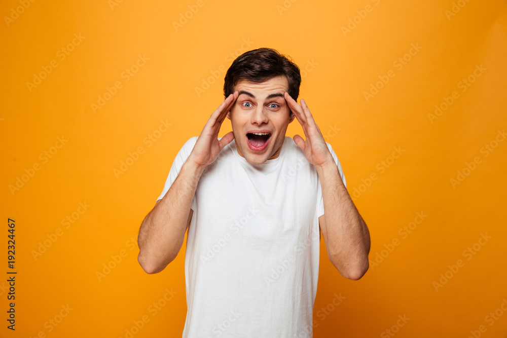 Surprised man in t-shirt holding head and looking at camera Surprised man in t-shirt holding head and looking at camera