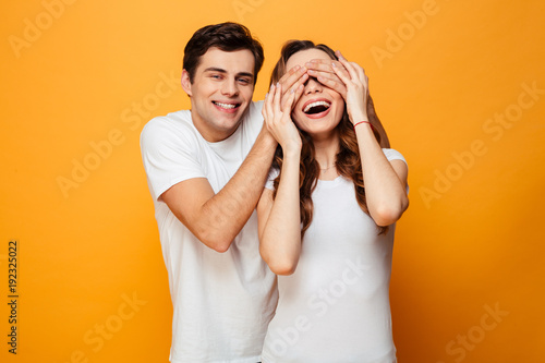 Image of man standing behind woman and covering her eyes