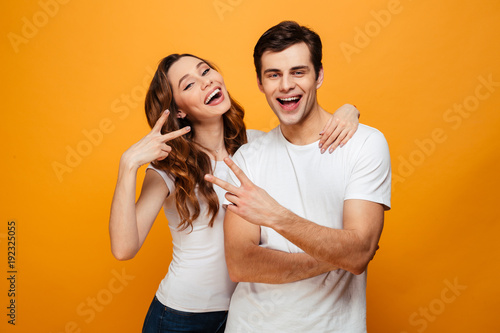 Cheerful young couple posing together while showing peace gestures