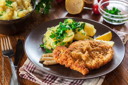 Bild auf Leinwand Homemade breaded viennese schnitzel with potato salad and asparagus on a plate