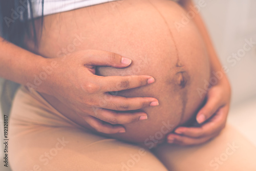 Young pregnant woman holds her hands on her no clothes swollen belly. Love concept. Horizontal with copy space. Pregnant women sitting and holding her belly of 8 months baby inside.