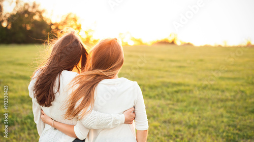 Photographie Young women in white sweaters are walking on the green field