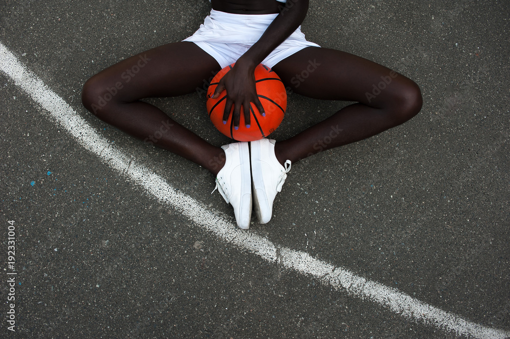 Naklejka premium Slim sporty afro-american girl and orange basketball at stadium