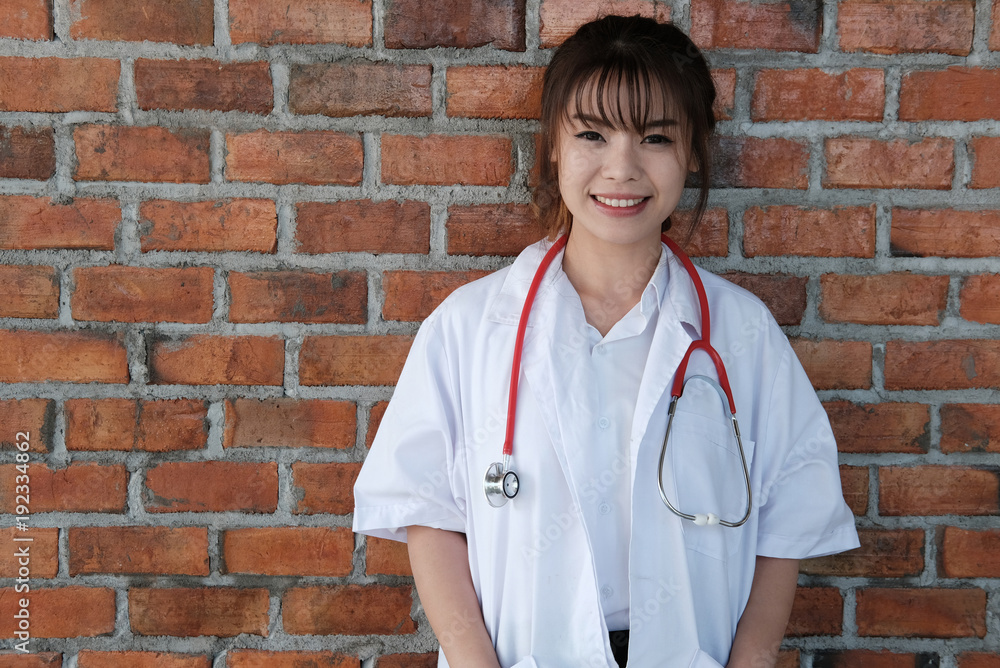 Confident young female doctor smiling at camera. Portrait of medical staff, physician or practitioner standing against brick wall Confident young female doctor smiling at camera. Portrait of medical staff, physician or practitioner standing against brick wall