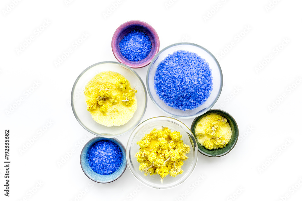 Colorful spa salt. Yellow spa salt with delicate spring flowers and violet lavender spa salt on white background top view copy space Colorful spa salt. Yellow spa salt with delicate spring flowers and violet lavender spa salt on white background top view copy space