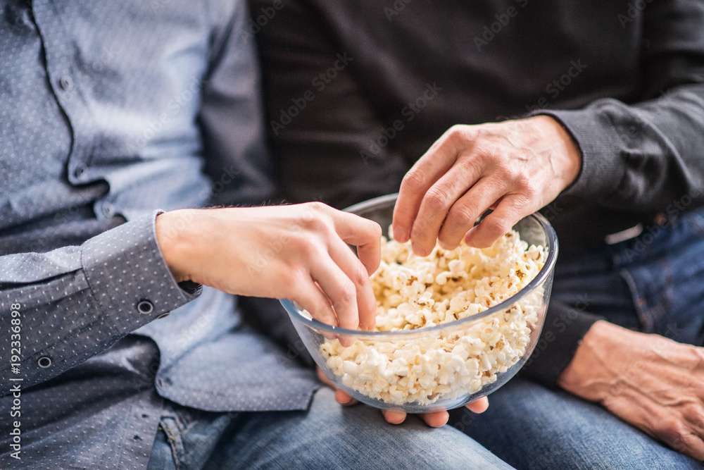 Son and his senior father eating popcorn at home. Son and his senior father eating popcorn at home.