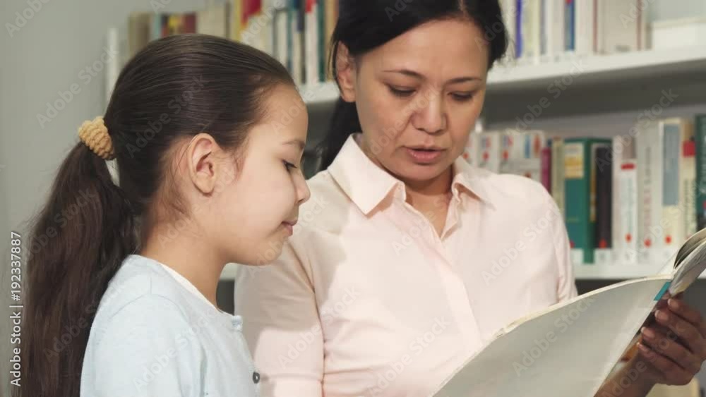 Beautiful woman and her little daughter reading a book at the library Beautiful woman and her little daughter reading a book at the library
