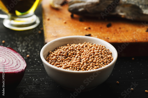 White mustard seeds in a white ceramic bowl on a wooden cutting board. Cooking process