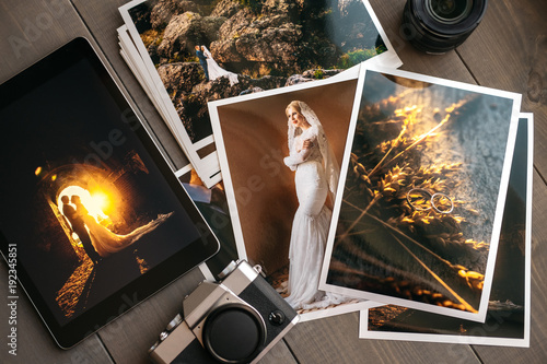 Printed wedding photos with the bride and groom, a vintage black camera and a black tablet with a picture of a wedding couple