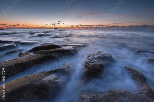 scenic view of sunset seascape with rocks covered by green moss on the ground.