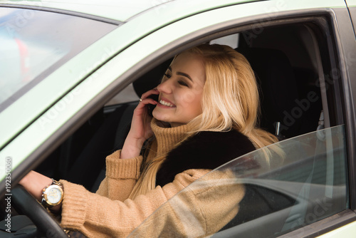 Beautiful happy girl in car using her smartphone