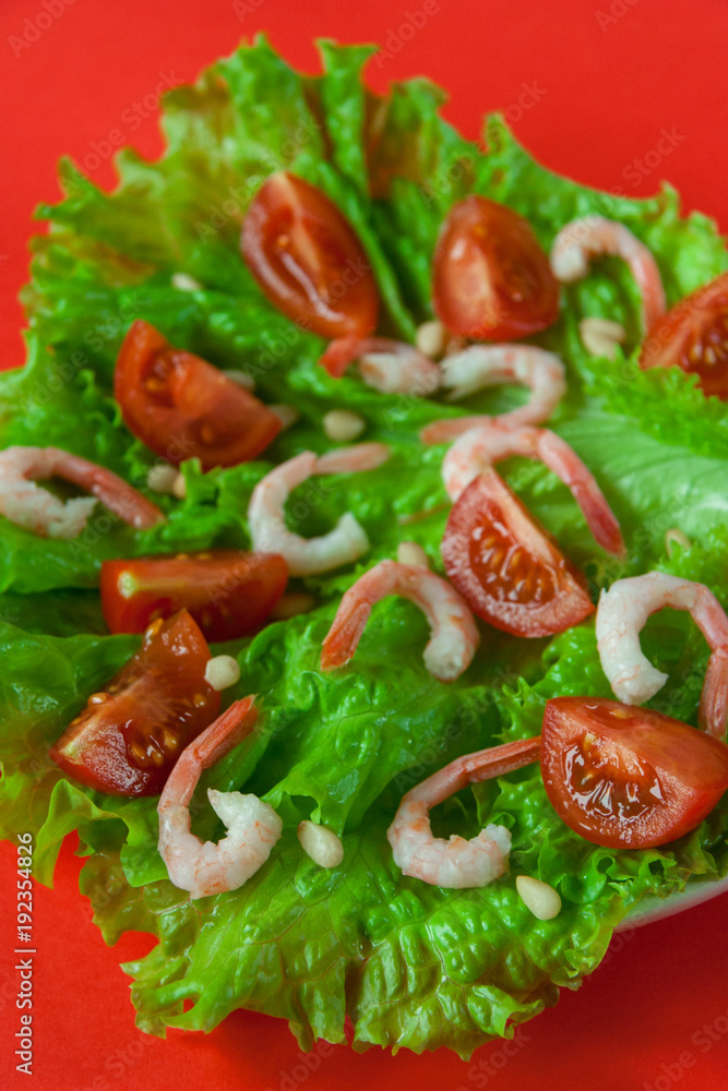 Salad of peeled shrimps and cherry tomatoes served on a leaf of fresh lettuce. Mediterranean Kitchen. Serving option. Close-up. Red background. Salad of peeled shrimps and cherry tomatoes served on a leaf of fresh lettuce. Mediterranean Kitchen. Serving option. Close-up. Red background.