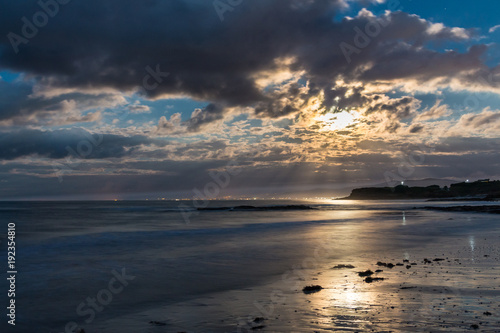 the full moon tries to peek through the clouds in the warm summer night from the beach of Foz  spain