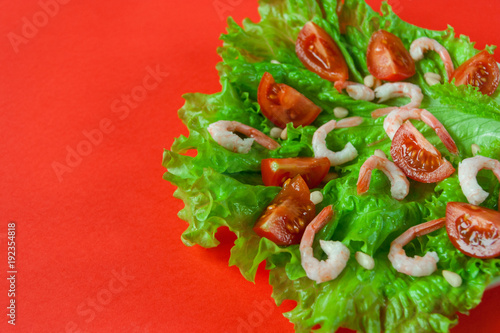 Salad of peeled shrimps and cherry tomatoes served on a leaf of fresh lettuce. Mediterranean Kitchen. Serving option. Close-up. Red background. With place for text. 