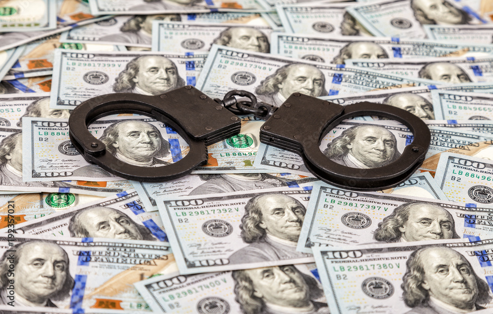 Steel black handcuffs lying on the background of american dollars Steel black handcuffs lying on the background of american dollars