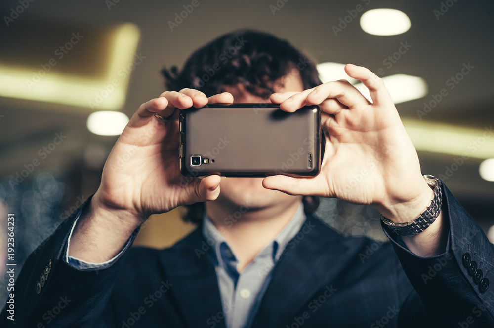 Business man looking at smartphone screen. Guy hides behind the mobile phone. Smartphones have entered our lifestyle.