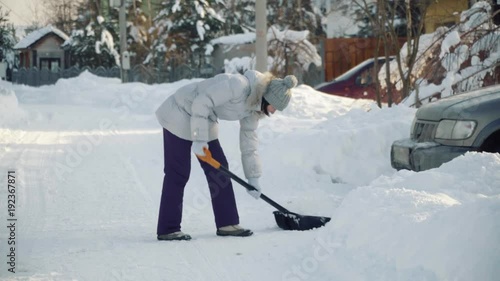 Young woman cleans snow by shovel for car in suburbs in winter.