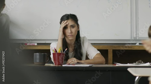 Frustrated teacher sitting at desk watching children in chaotic classroom / Provo, Utah, United States
